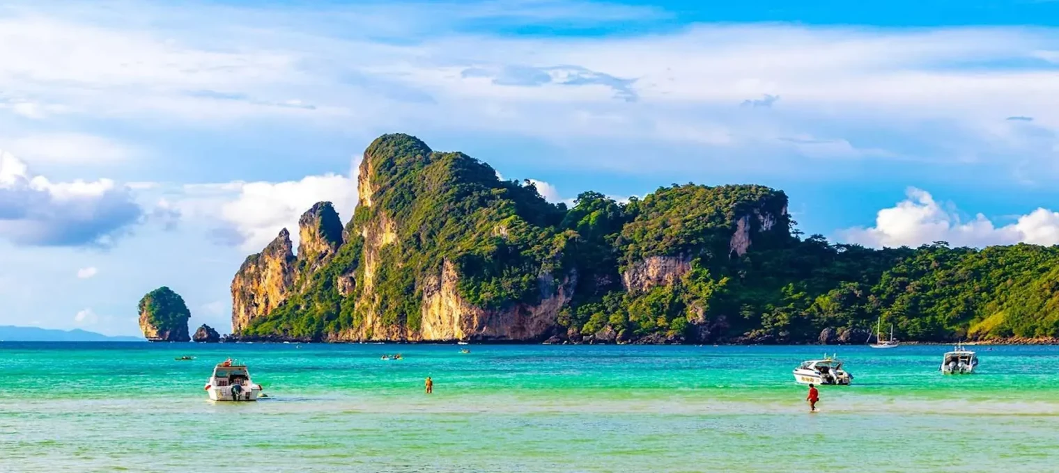 Beautiful turquoise waters with boats near lush green islands in Phuket, Thailand.