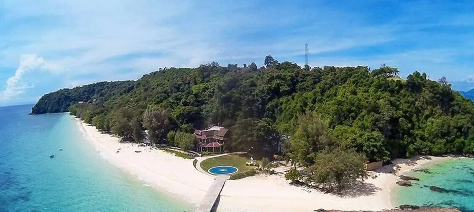 Scenic view of a lush island in Phuket with a beach, clear water, and a swimming pool.