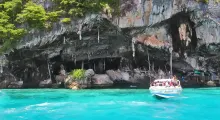 Boat approaching rocky cave entrance near lush green cliffs in Phuket's turquoise waters.