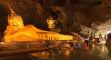 Golden reclining Buddha statue in a cave temple in Phuket, Thailand, with serene lighting.