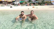 Two men enjoying the clear waters at a Phuket beach, surrounded by colorful umbrellas.