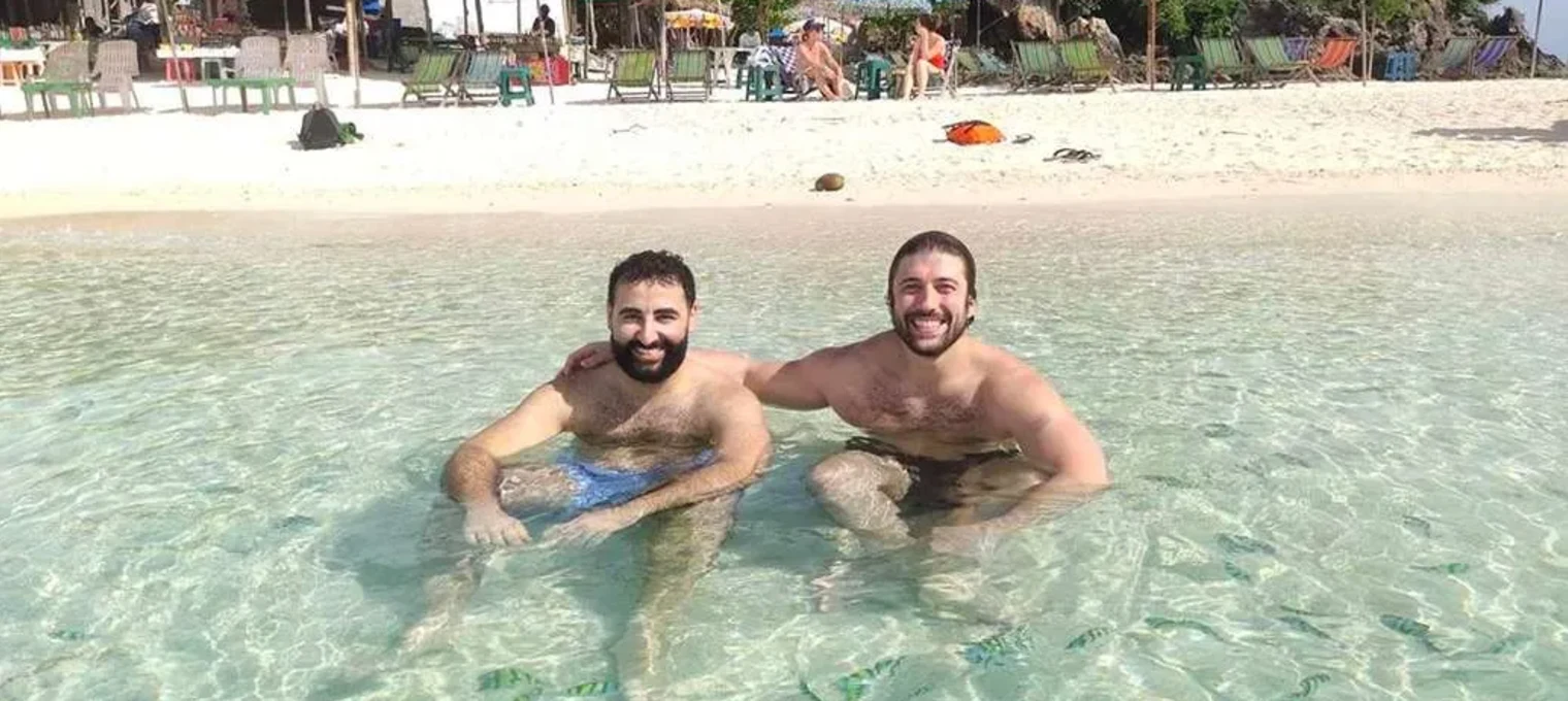 Two men enjoying the clear waters at a Phuket beach, surrounded by colorful umbrellas.