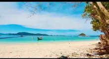 A serene beach in Phuket with clear turquoise water and a longtail boat.