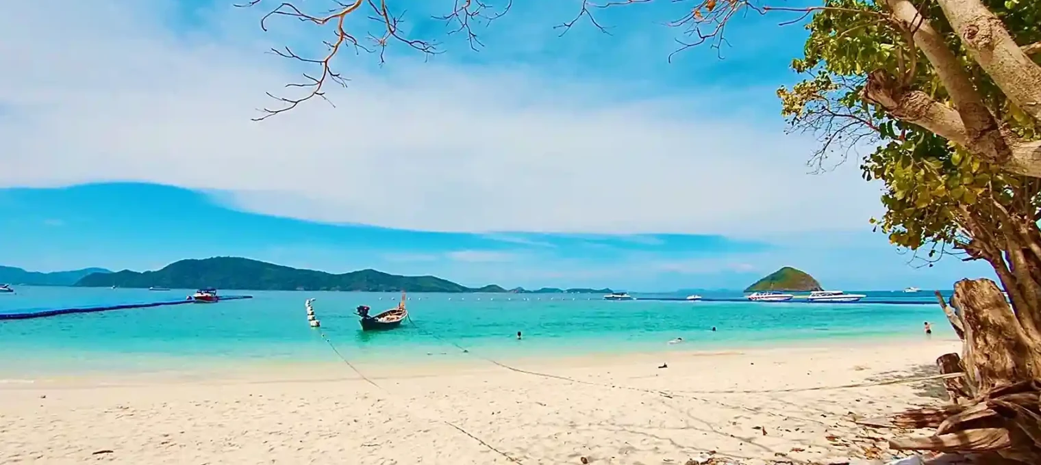 A serene beach in Phuket with clear turquoise water and a longtail boat.