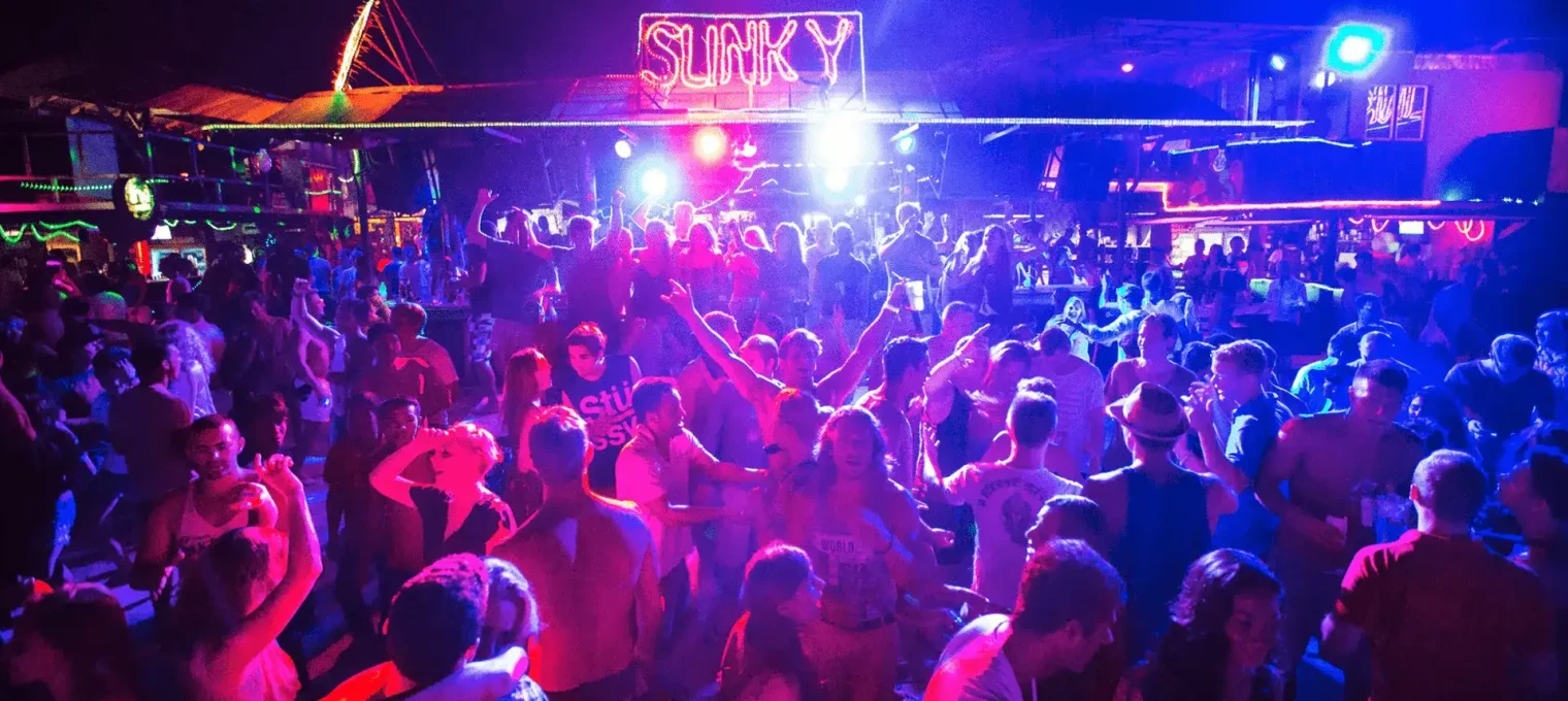 Crowd dancing at a vibrant night club in Phuket, illuminated by colorful lights.