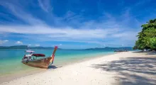 Wooden boat on a sandy beach with turquoise water and blue sky in Phuket.