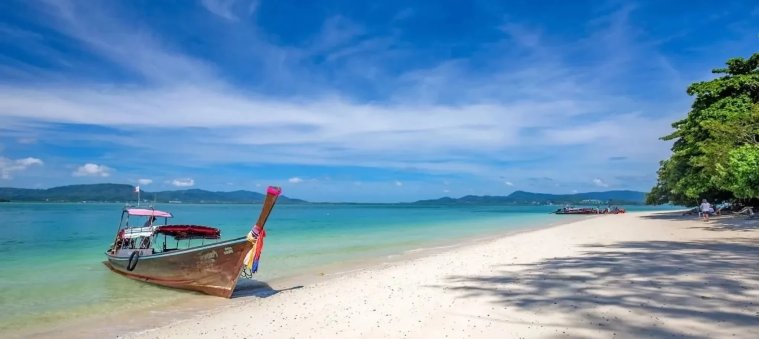 Wooden boat on a sandy beach with turquoise water and blue sky in Phuket.