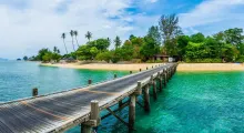 Wooden pier extending over clear blue water in Phuket, with lush greenery in the background.