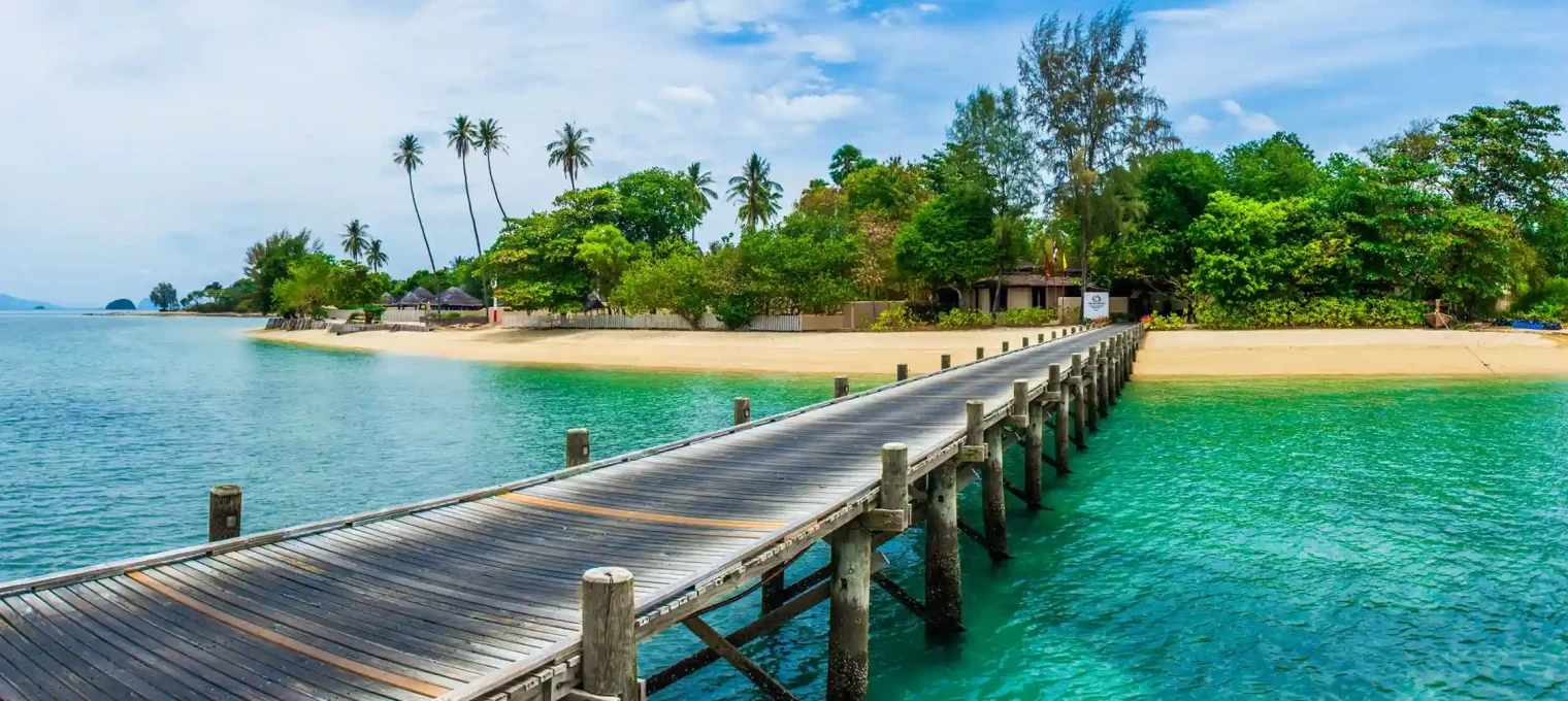 Wooden pier extending over clear blue water in Phuket, with lush greenery in the background.