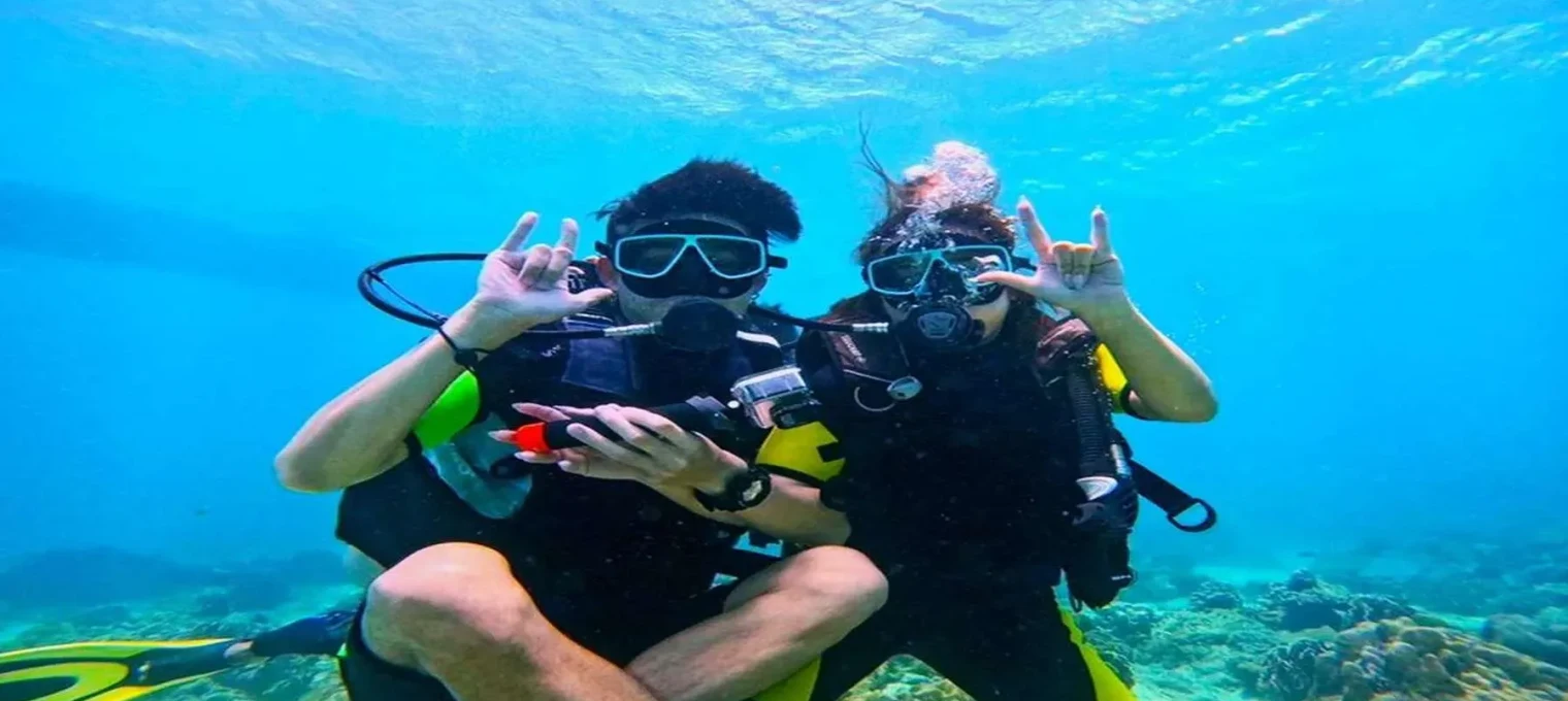 Two divers giving hand signals underwater in Phuket's clear blue waters.