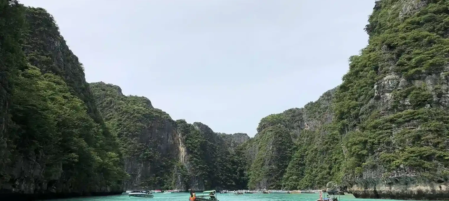 Scenic view of lush cliffs and turquoise waters in Phuket, Thailand, with boats.