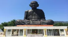 Giant seated statue of a monk in Phuket, surrounded by palm trees and a clear blue sky.