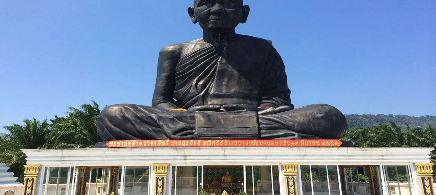 Giant seated statue of a monk in Phuket, surrounded by palm trees and a clear blue sky.