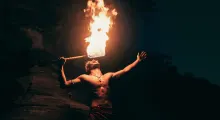 Fire performer striking a dramatic pose while breathing fire in Phuket at night.