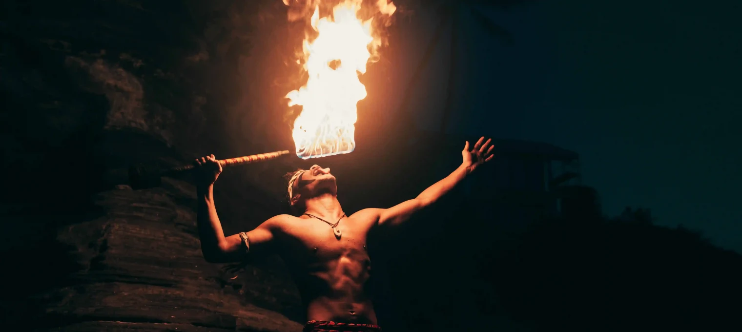 Fire performer striking a dramatic pose while breathing fire in Phuket at night.