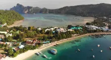 Aerial view of Phuket's coastline, featuring lush green hills and boats in the clear blue water.