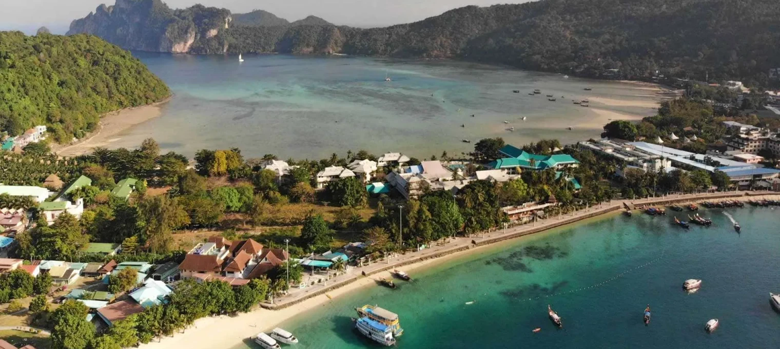 Aerial view of Phuket's coastline, featuring lush green hills and boats in the clear blue water.