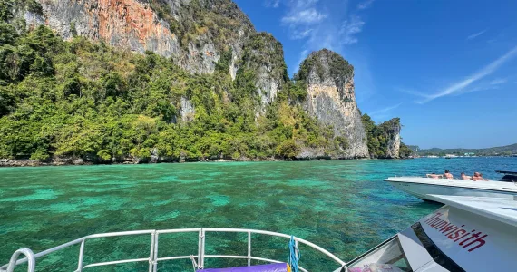 Scenic view from a boat in Phuket, showcasing green waters and rocky cliffs.