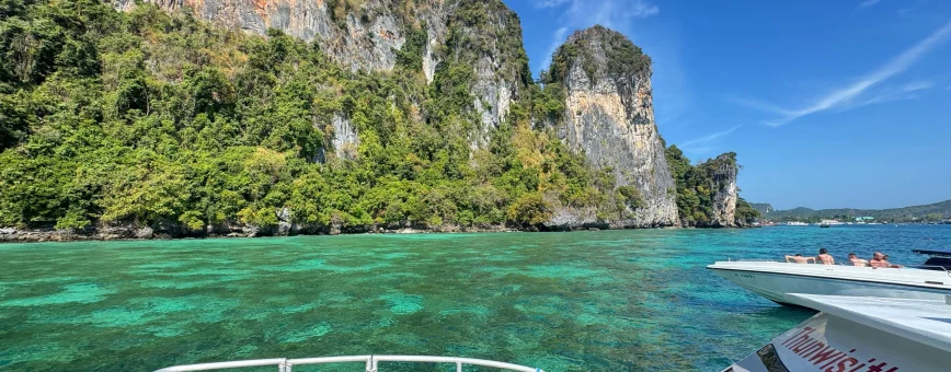 Scenic view from a boat in Phuket, showcasing green waters and rocky cliffs.