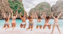 Group of women in swimwear jumping joyfully at a beach in Phuket.