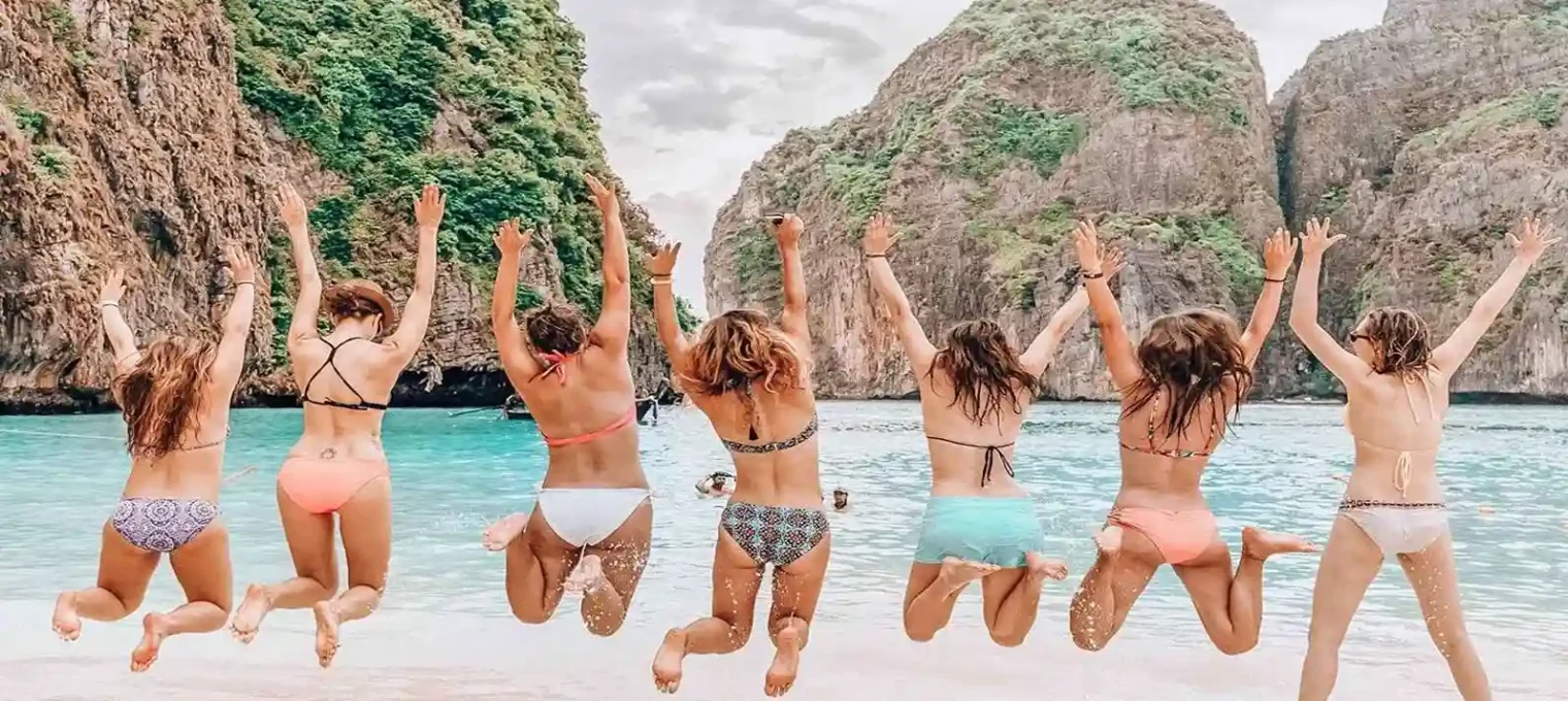 Group of women in swimwear jumping joyfully at a beach in Phuket.