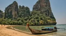 Longtail boat on a beach in Phuket with lush rock formations in the background.