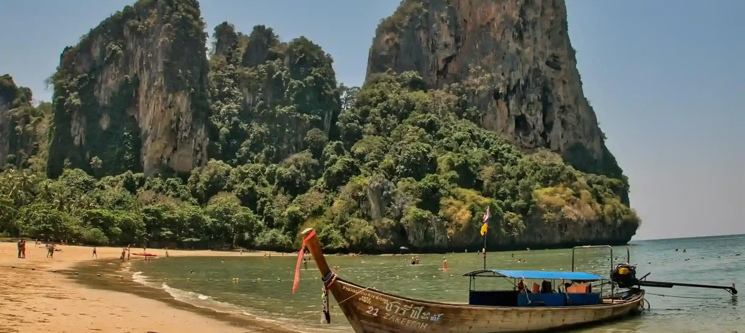 Longtail boat on a beach in Phuket with lush rock formations in the background.
