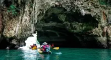 Kayakers navigating through a rocky cave in Phuket's turquoise waters.