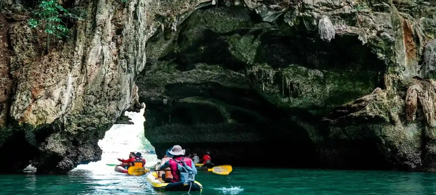 Kayakers navigating through a rocky cave in Phuket's turquoise waters.