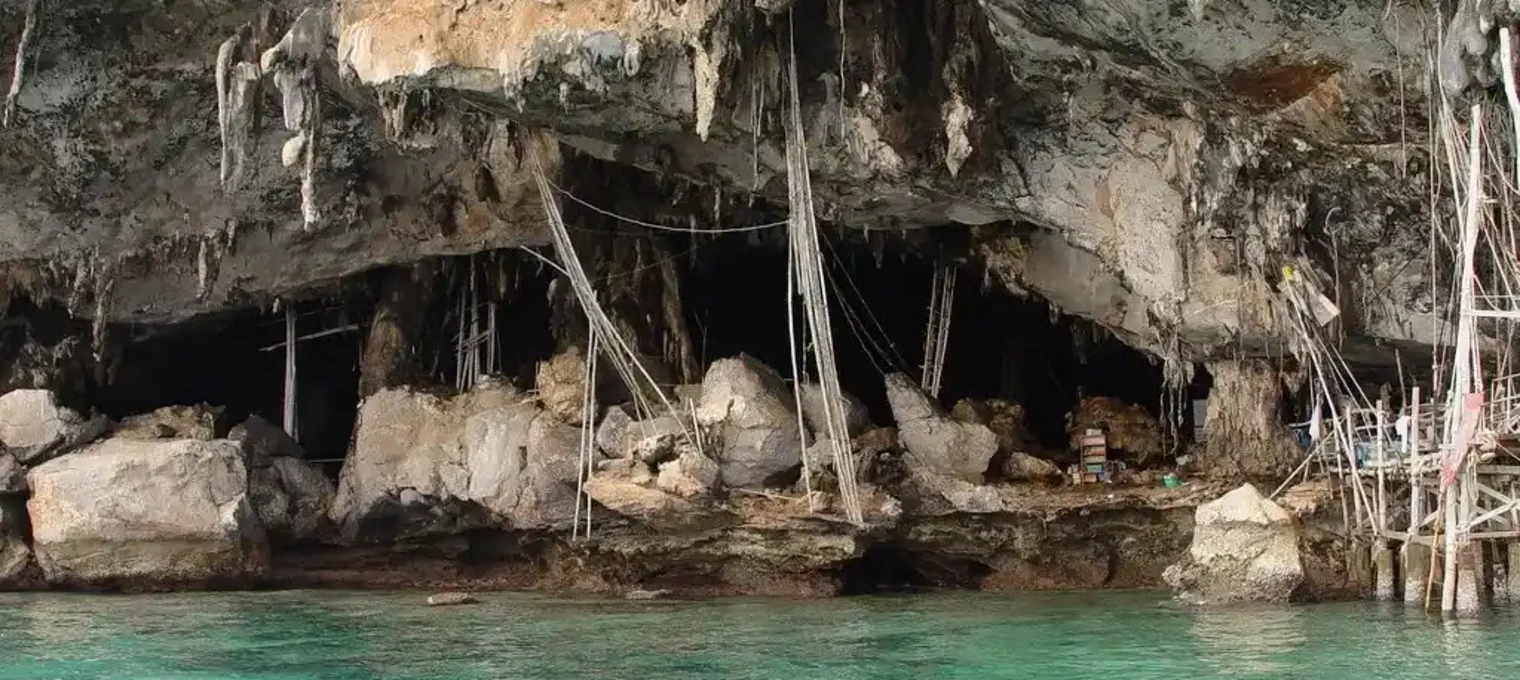 Rocky cave entrance by clear turquoise water in Phuket, Thailand.
