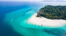 Aerial view of a tropical beach in Phuket with clear blue water and boats anchored nearby.