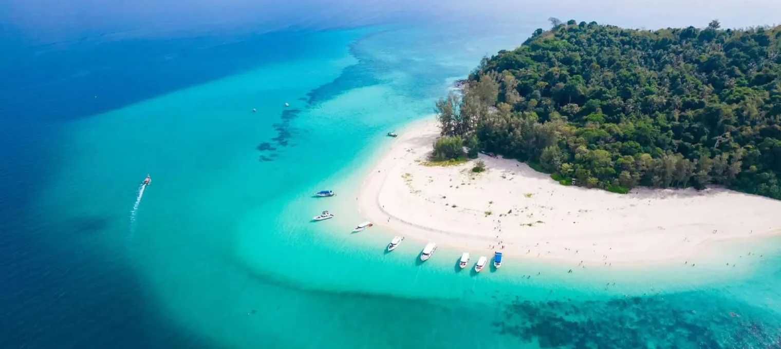 Aerial view of a tropical beach in Phuket with clear blue water and boats anchored nearby.