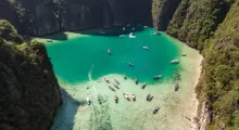Aerial view of turquoise bay in Phuket, dotted with boats and surrounded by cliffs.