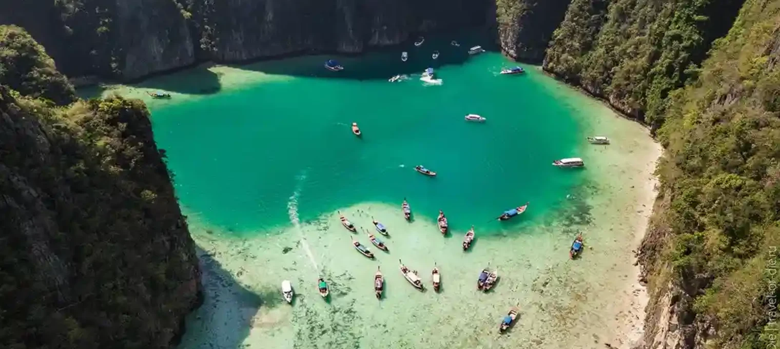 Aerial view of turquoise bay in Phuket, dotted with boats and surrounded by cliffs.