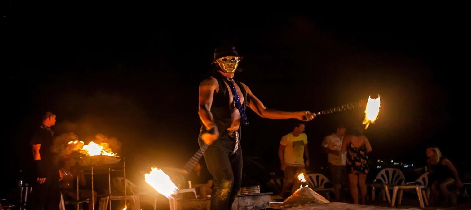 Fire dancer performing at night on a beach in Phuket, surrounded by an enthusiastic audience.