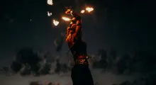 Fire performer dancing at sunset in Phuket, swirling flaming torches against a dark sky.
