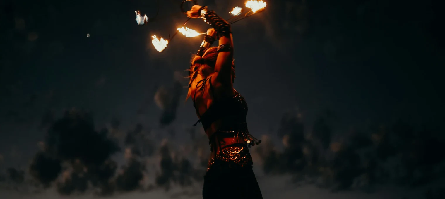 Fire performer dancing at sunset in Phuket, swirling flaming torches against a dark sky.
