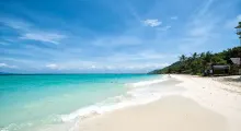 Pristine beach in Phuket with clear turquoise water and a sunny blue sky.