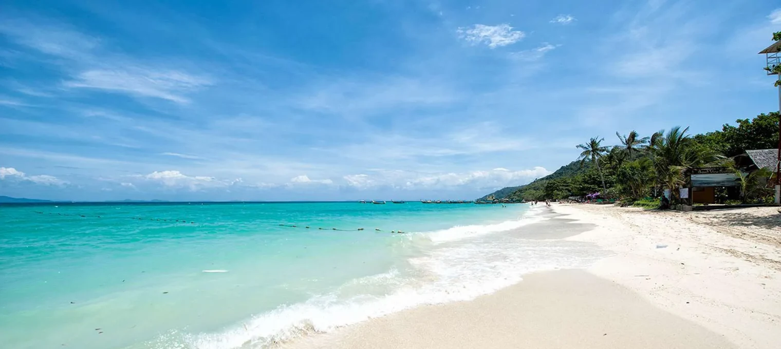 Pristine beach in Phuket with clear turquoise water and a sunny blue sky.
