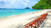 Secluded beach in Phuket with wooden loungers and turquoise water under a blue sky.