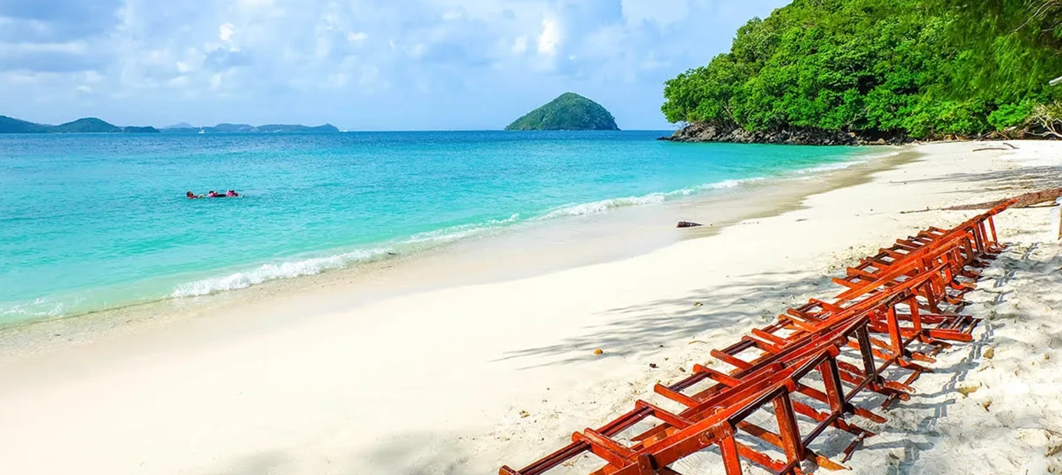 Secluded beach in Phuket with wooden loungers and turquoise water under a blue sky.