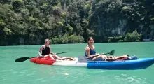 Two women kayaking in turquoise waters surrounded by lush greenery in Phuket.