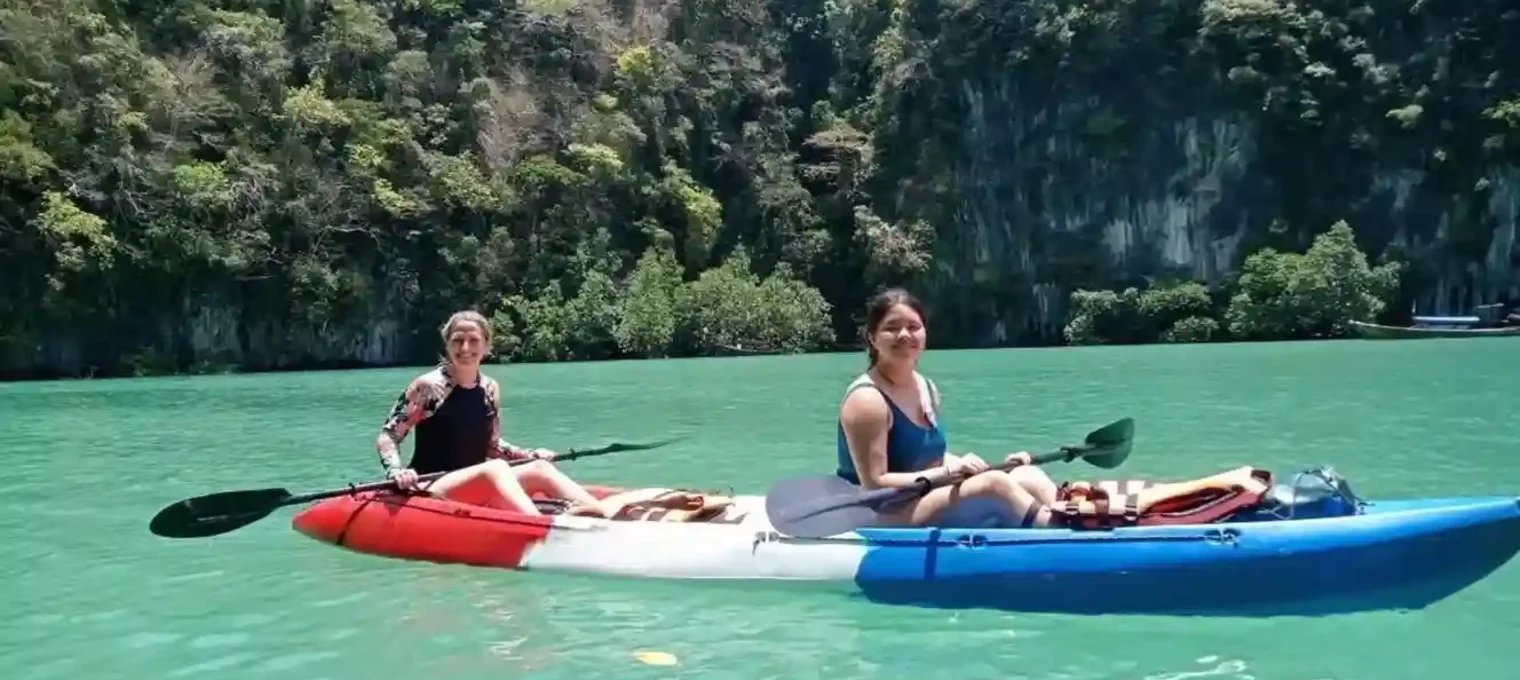 Two women kayaking in turquoise waters surrounded by lush greenery in Phuket.