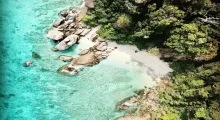 Aerial view of a secluded beach with clear turquoise waters and rocky shoreline in Phuket.