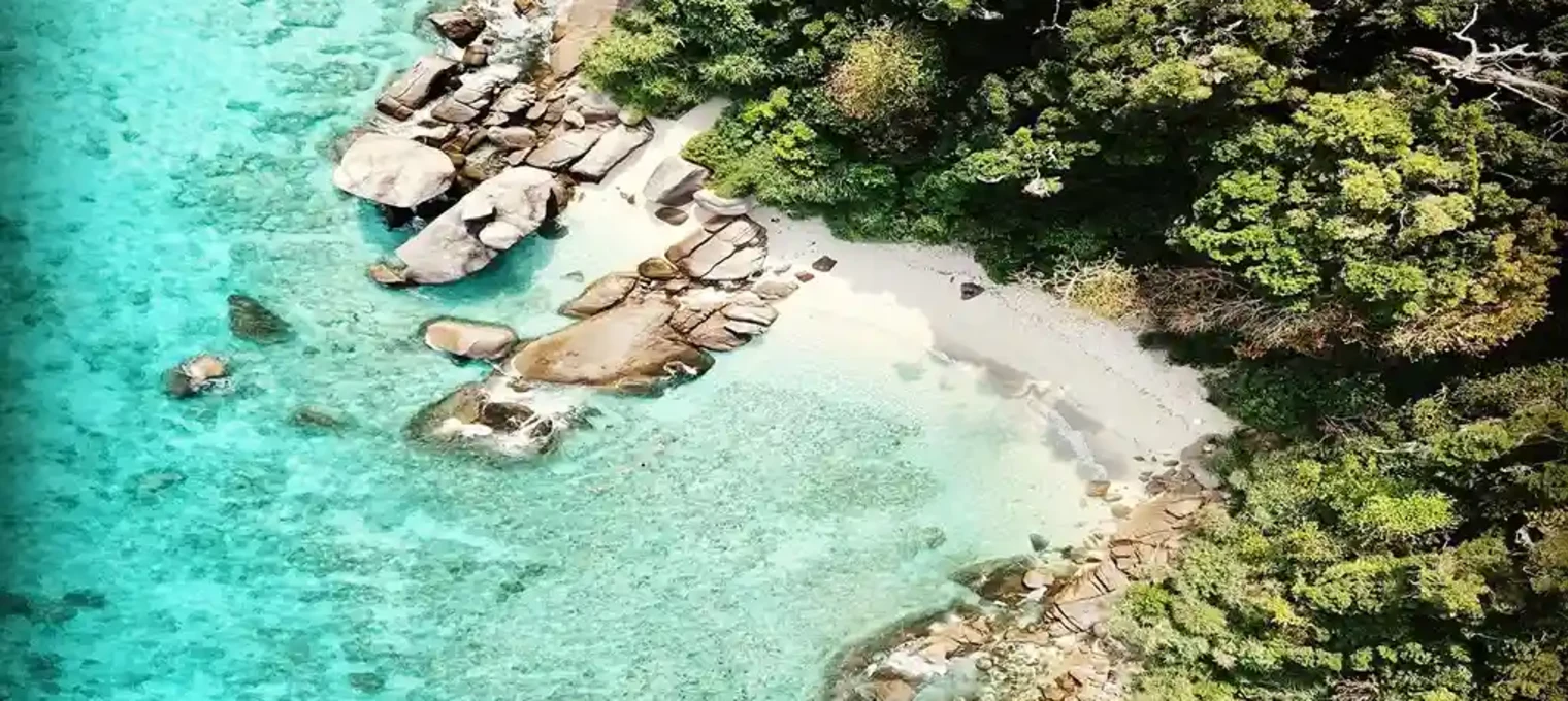 Aerial view of a secluded beach with clear turquoise waters and rocky shoreline in Phuket.