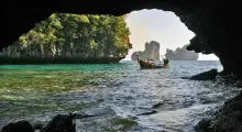 A scenic view from a cave in Phuket, featuring a boat on crystal-clear waters and lush cliffs.
