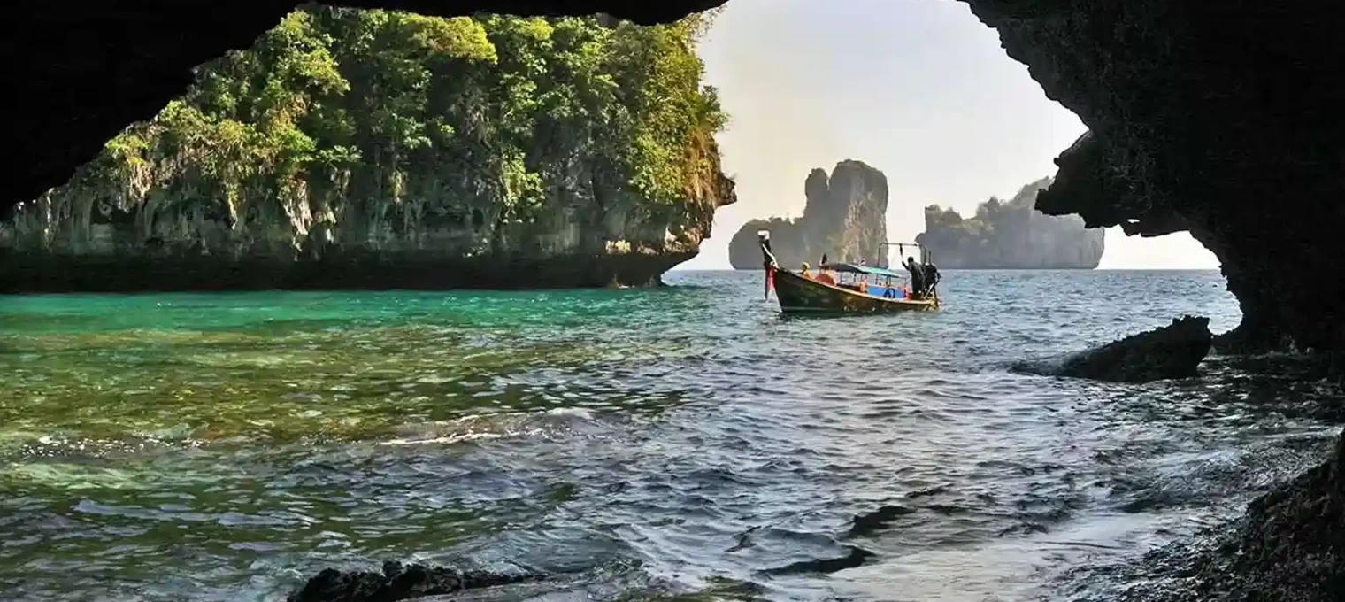 A scenic view from a cave in Phuket, featuring a boat on crystal-clear waters and lush cliffs.