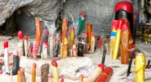 Colorful wooden phallic sculptures scattered on sandy ground in a cave in Phuket.