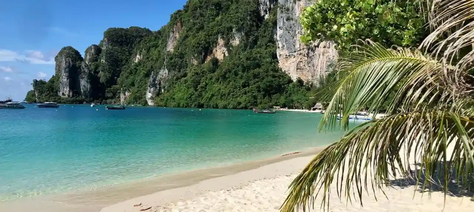Beautiful beach in Phuket with turquoise waters, sandy shore, and lush green cliffs.