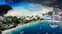 Aerial view of Phuket's coastline with boats, beach, and lush green mountains.